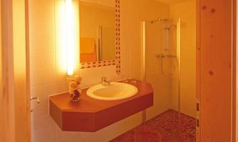 A modern bathroom with bright lighting and a shower. The walls are tiled in light colors, and the floor is made of decorative tiles.