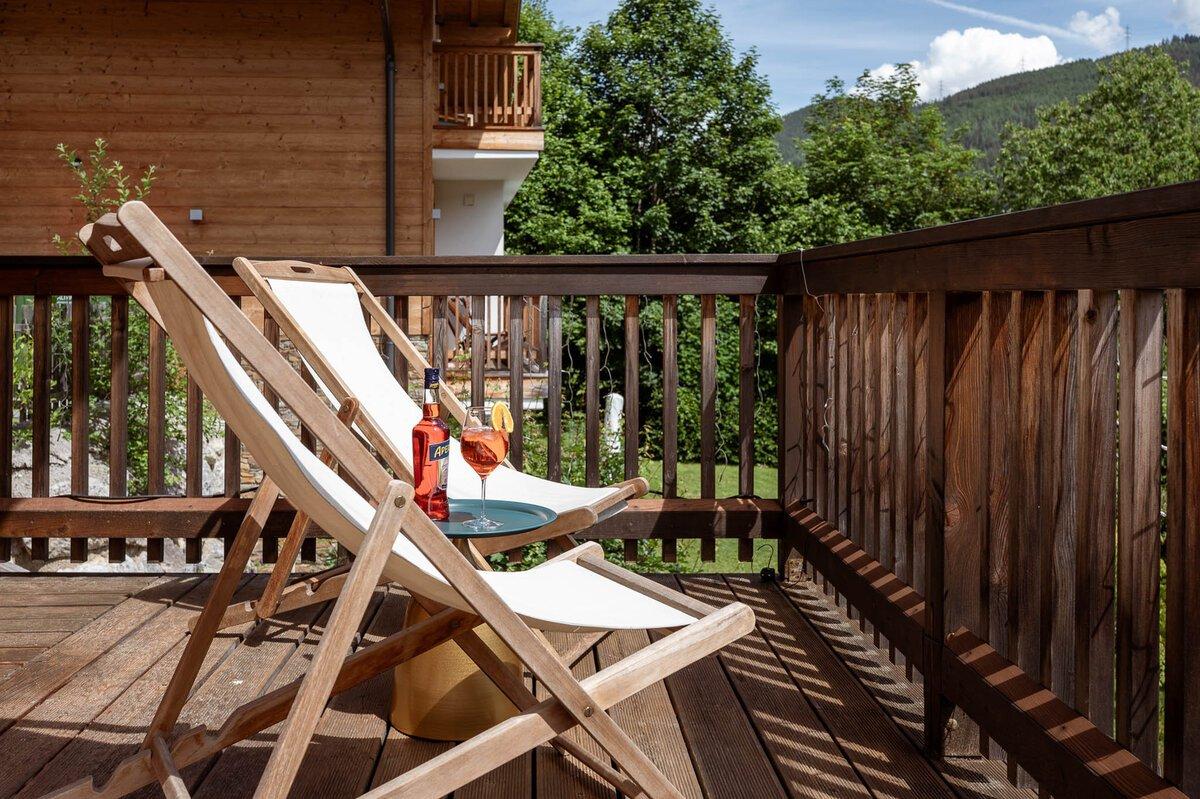 A cozy balcony with two lounge chairs and a small table. In the background, trees and a beautiful landscape can be seen.