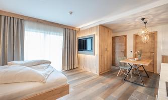 A modern room with wooden furniture and large windows. There is a bed, a table, and a cozy atmosphere.