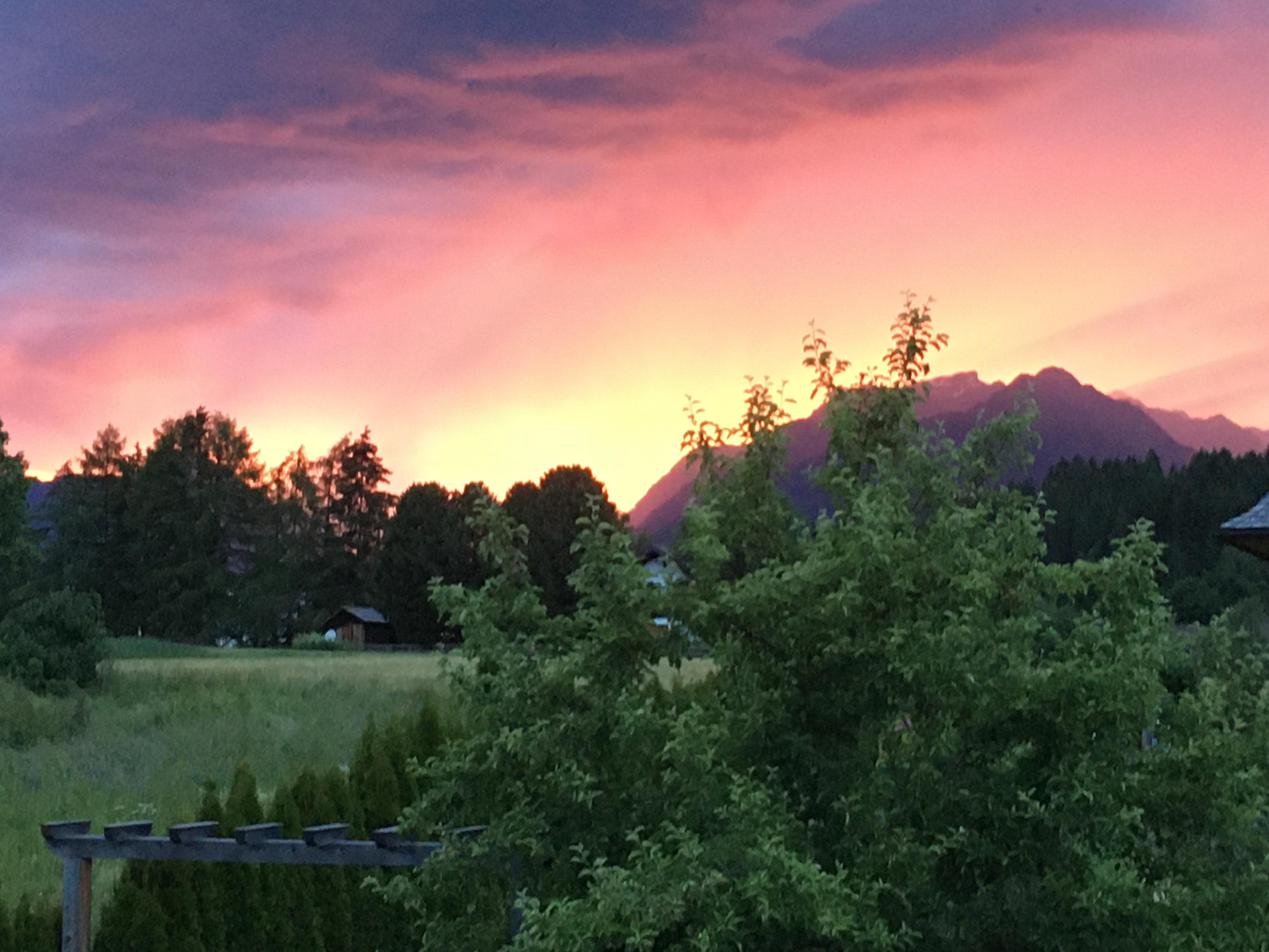 A breathtaking landscape at sunset with vibrant colors in the sky. In the foreground, there are trees and a meadow.