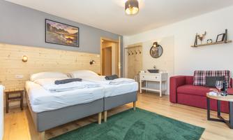 A modern room with a double bed and a cozy red sofa. The space features wooden floors and decorative elements on the walls.