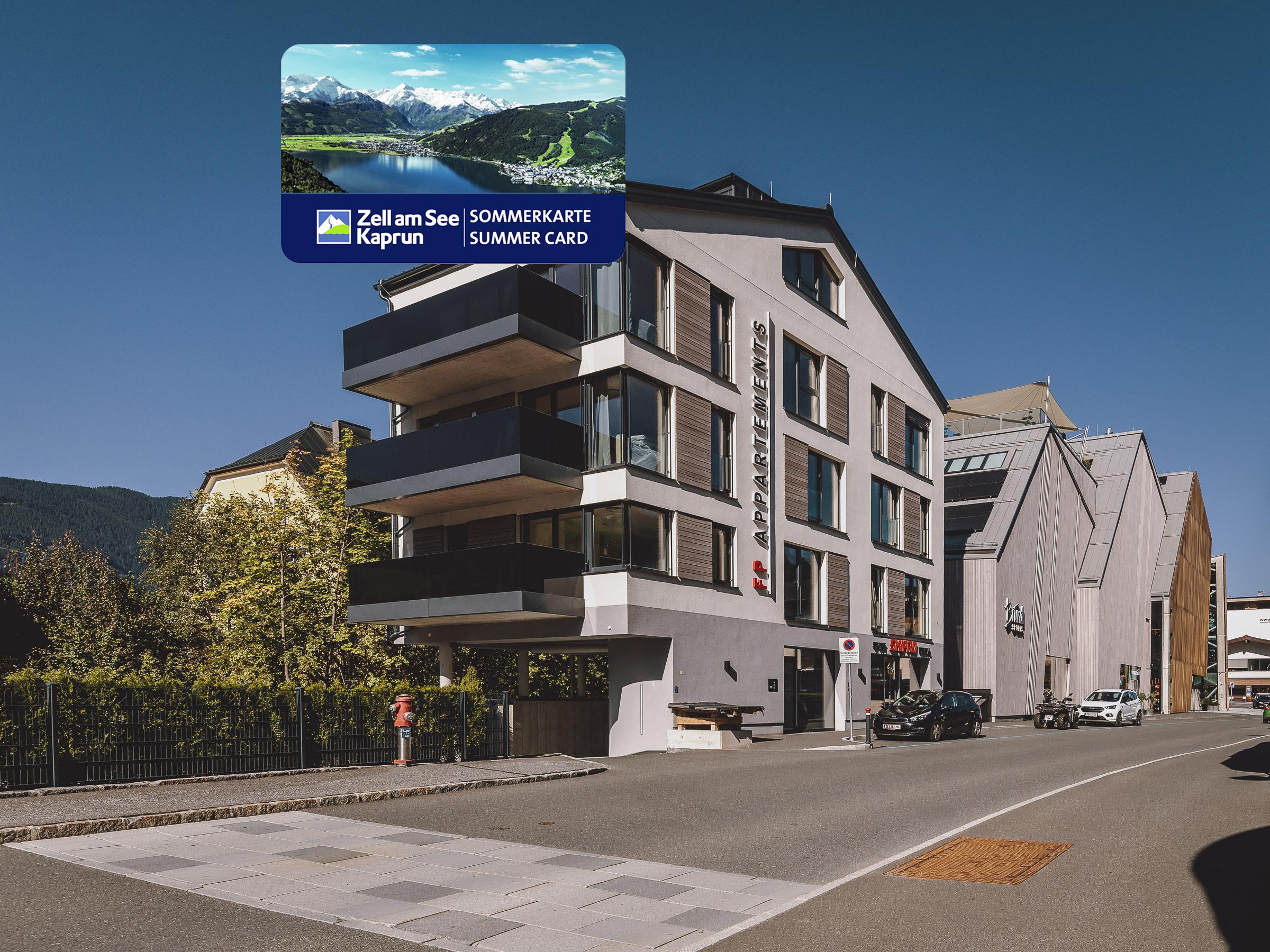 A modern building on a street with clean lines and large windows. In the foreground is information about the summer card for Zell am See Kaprun.