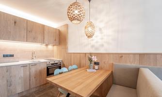 A modern kitchen with wooden cabinets and a cozy dining area. The warm light sources create an inviting atmosphere.