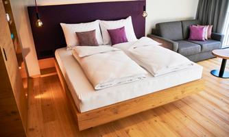 A modern bedroom with a large bed and soft pillows. Next to the bed is a cozy couch and a small table.