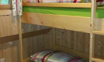 A cozy room with a wooden bunk bed. The bedding is colorful and there is a carpet on the wooden floor.