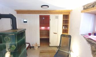 A cozy sauna area with a traditional stove and an armchair. The wooden paneling and warm light create a relaxing atmosphere.