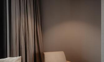 A modern living room with a bright sofa and a comfortable armchair. The room has gray curtains and a simple, elegant atmosphere.