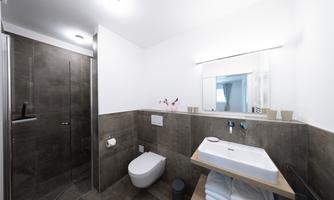 A modern bathroom with a shower, sink, and elegant tiles. The decor is simple and functional, with towels on a shelf.