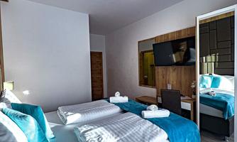 A modern bedroom with a double bed and bright pillows. The walls are painted in neutral colors, and a mirror reflects the decor.