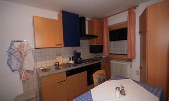 A cozy kitchen with wooden furniture and a table set with a blue tablecloth. Cooking utensils are on the countertop and a stove is present.