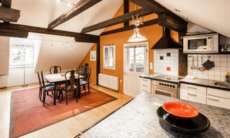 A modern kitchen with wooden beams and a large dining table. The walls are painted in warm colors and the light is bright and inviting.
