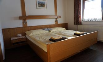 A cozy bedroom with a large double bed and light wood. There is a window with curtains and a small picture on the wall.
