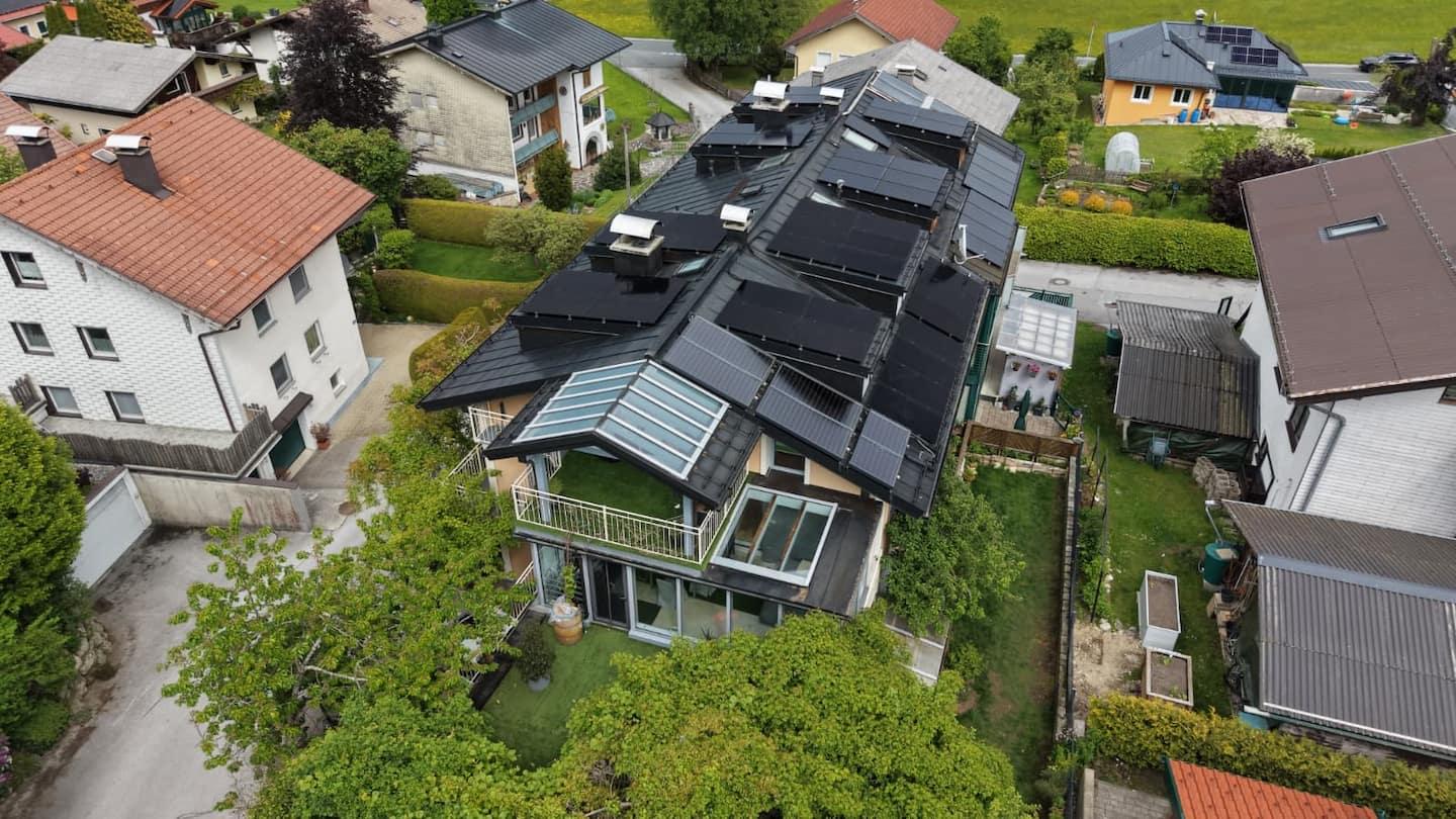 A modern residential house with solar panels on the roof.  
Surrounded by gardens and other single-family homes.