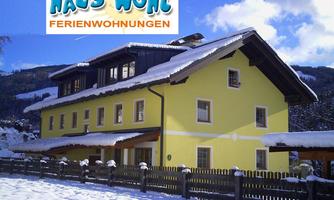 A cozy yellow holiday home in the snow. The surrounding landscape is mountainous and wintry.