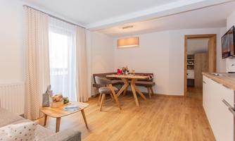 A modern living room with a dining table and chairs. Bright windows provide plenty of daylight and an inviting atmosphere.
