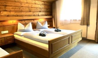 A cozy bedroom with wooden walls and two beds. Pillows are placed on the beds, and a window provides daylight.