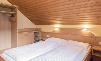 A cozy bedroom with a double bed and a wood-paneled ceiling. There is a wardrobe and soft lighting for a relaxed atmosphere.