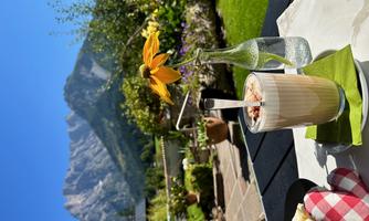 A glass with a delicious drink is sitting on a table outdoors. In the background, there is an impressive mountain landscape under a blue sky.