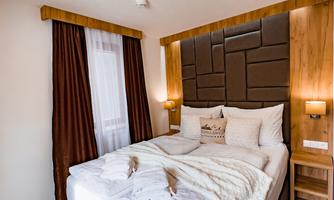 A cozy bedroom with a large bed and elegant wood paneling. Soft light filters into the room through the windows.