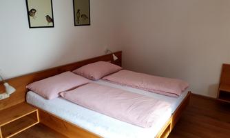 A simple bedroom with a wooden bed and two separate mattresses. On the wall, there are two pictures of birds.