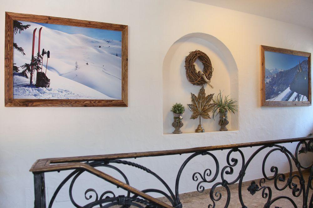 A cozy interior with rustic pictures of snowy mountains and skis. On the wall, decorative elements such as plants and a wreath can be seen.