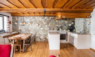 A modern kitchen with a stone wall and wooden ceiling. The dining area is cozy with a wooden table and chairs.