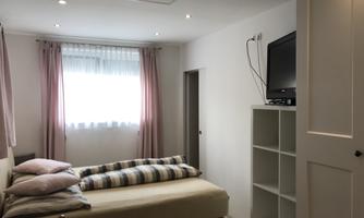 A cozy bedroom with a double bed and a television. Brightly lit by a window with curtains.
