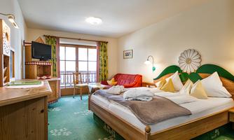 A cozy hotel room with a double bed and a red sofa. The decor is rustic with wood and a green carpet.