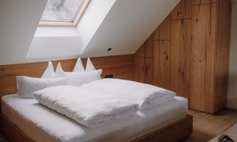 A cozy bedroom with a large bed and a skylight. The walls and furniture are made of light wood, creating a warm atmosphere.