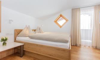 A modern bedroom with a cozy double bed and two pillows.  
Large windows let in plenty of light and the wooden floor creates a warm atmosphere.