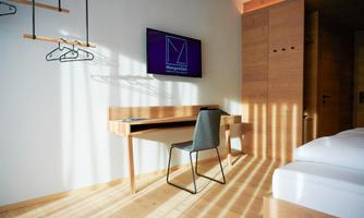 A modern room with a desk, a chair, and a television mounted on the wall. Rays of light gently fall onto the wooden floor.