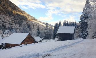 A winter landscape with snow-covered huts and trees. The sky is clear and the mountains are visible in the background.
