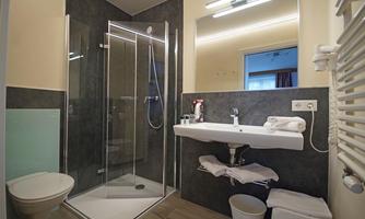 A modern bathroom with a shower and a sink. The walls are designed in gray and light shades, and there are towels on the sink.