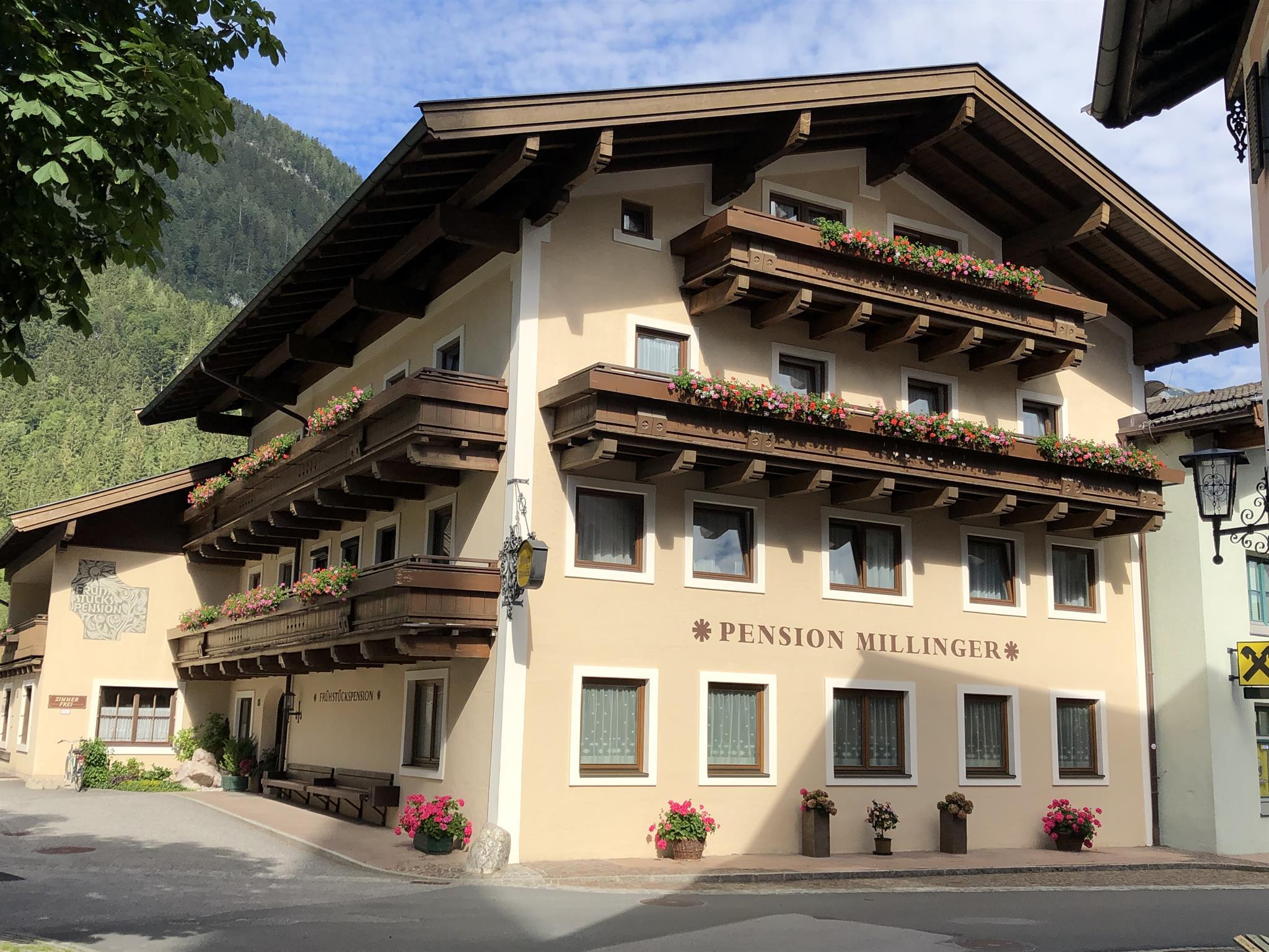 A cozy building with balconies that serves as a guesthouse. It is surrounded by mountains and has an inviting atmosphere.