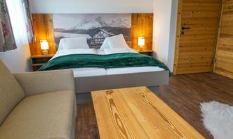 A cozy bedroom with a double bed and a wooden wardrobe. The room has a warm atmosphere with a comfortable sofa and a wooden table.
