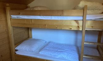 A bunk bed made of wood in a room. The bed has two mattresses with white bedding and pillows.