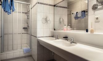 A modern bathroom with a shower and double sink. Towels are hanging on the wall and the ambiance is bright and clean.