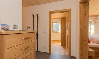 An inviting hallway with wood paneling and a dresser. Skis hang on the wall, and there is access to additional rooms.