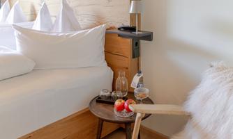 A cozy room with a bed and a small table. On the table are a few apples and a glass of water.