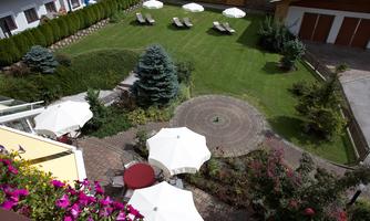 A well-maintained garden with green lawn area and loungers. Colorful flowers and sun umbrellas surround the seating.
