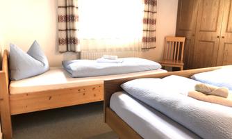 A bright bedroom with two single beds and a wooden chair. The windows let in plenty of natural light.