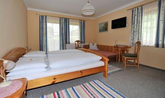 A cozy bedroom with a double bed and a small table. Large windows let in plenty of light and give the room an inviting atmosphere.