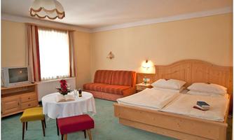 A cozy room with a double bed, a seating area, and a small table. The walls are painted in soft colors, and there is plenty of natural light from a window.