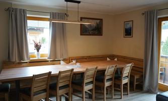 A cozy dining area with a long wooden table and chairs. The window lets in a lot of daylight and is adorned with curtains.