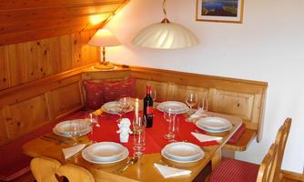 A cozy dining area with a wooden table, set with white dishes and red wine. The walls are made of wood and a warm lamp provides inviting light.