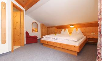 A cozy bedroom with wooden decor and a large double bed. A red armchair and a mirror complete the room.