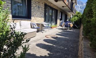 An inviting terrace with upholstered furniture and a small table. In the background, trees and mountain peaks are visible.