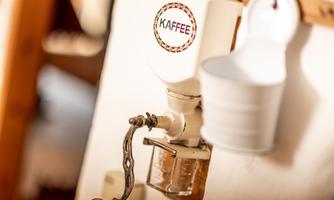 An old coffee grinder on the wall with the inscription "COFFEE". Next to it hangs a white measuring cup.
