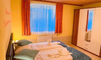 A cozy bedroom with a double bed and fresh towels. The room has large windows, a wooden ceiling, and warm colors.