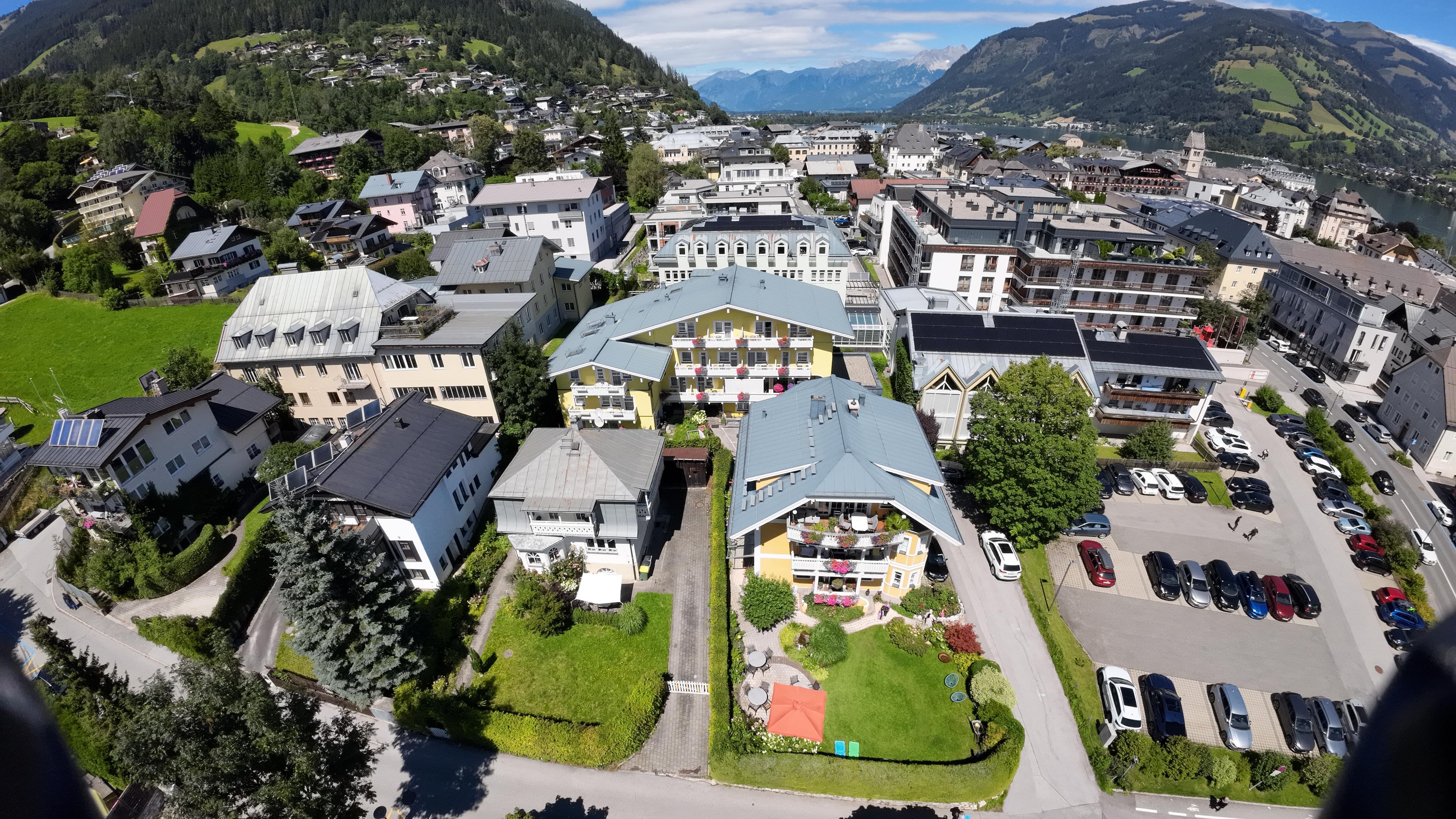 An aerial view of a city with a mix of residential buildings and shops. In the background, mountains and green countryside can be seen.
